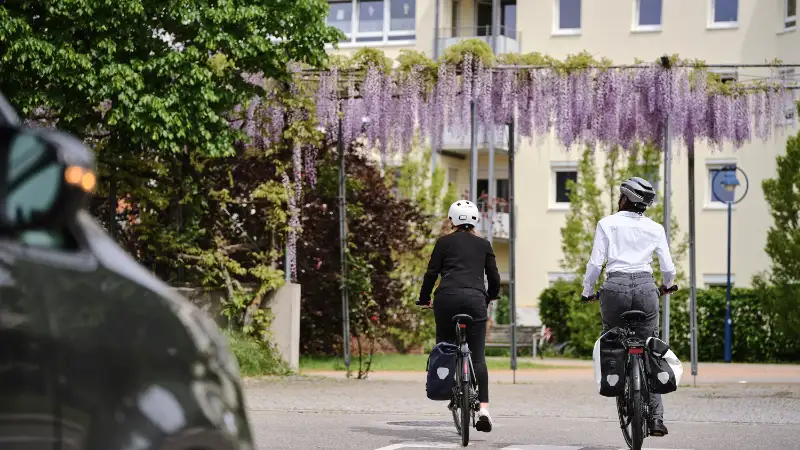 Zwei Jobradlerinnen fahren vom Betrachter weg auf ein Mietshaus zu.