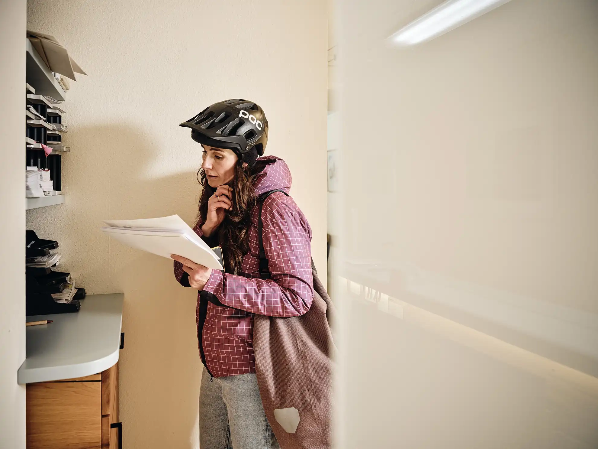 Eine Frau mit Fahrradhelm ist gerade im Büro angekommen und öffnet Post